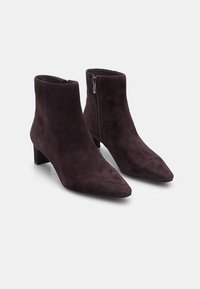 Botas de tobillo de ante marrón con punta afilada y tacón cuadrado. Presentan una cremallera lateral. Textura suave y diseño minimalista.