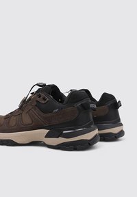 Chaussures de sport brun et noir avec une tige en mesh et suède, semelle en caoutchouc, accents texturés et un système de laçage rapide. Onglet de tirage à l'arrière inclus.