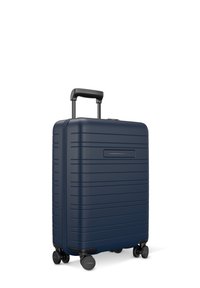 Valise rigide bleu marine avec des bandes horizontales texturées, quatre roulettes à rotation fluide et une poignée rétractable. Design simple sans accents visibles.