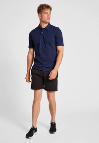Navyblauw poloshirt met korte mouwen en een kraag, gemaakt van gladde stof. Gecombineerd met zwarte shorts en sportschoenen.
