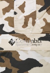Tissu à motif camouflage en beige, marron et noir. Présente le logo de Columbia Sportswear Company, des détails cousus, et une texture lisse.