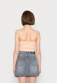 Top cropped smock listrado em laranja e branco com alças finas, combinado com uma saia mini A-line de denim cinza com bainha desfiada e bolsos traseiros.
