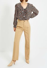 Blusa nera fluida con motivo floreale colorato, scollatura a V e maniche lunghe; abbinata a pantaloni beige a vita alta e gamba larga e sandali nude.