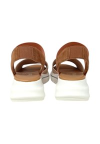 Sandali in suede marrone con suola bianca imbottita. Design aperto dietro con cinturini elastici per supporto. Superficie interna liscia, stile minimalista.