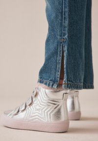 Silver metallic högskor med stjärnmönster, i kombination med blå denimjeans med sidofickor och rosa plyschfoder i nederkant.