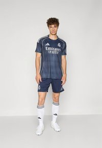 Tumesinise jalgpallivormi komplekt, millel on logo, õhukesed kollased õmblused ja valged detailid; sisaldab särki, pükse ja põlvikukõrguseid triibulisi sokke.