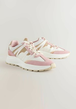 Rozā un baltie sporta apavi ir izgatavoti no zamša un acs materiāliem, tiem ir noapaļota purngala forma un teksturēti akcenti sānos un uz auklām.