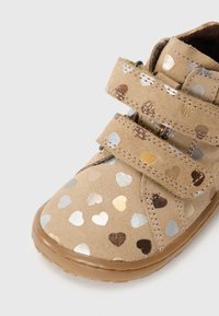 Scarpa in suede beige con motivi a forma di cuore in argento, oro e marrone, fissata da due strap in velcro; suola in gomma con grip testurizzato; design con punta arrotondata.