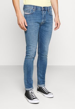 Jeans de mezclilla azul con un corte ajustado, que cuentan con bolsillos delanteros y dobladillos enrollados, combinados con zapatillas en blanco y negro. Textura suave.