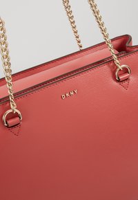Sac à main en cuir corail rose DKNY avec bandoulières chaîne dorées et petit logo doré DKNY sur le panneau avant.