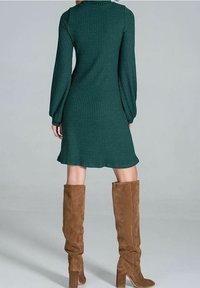 Grünes geripptes langärmliges Kleid mit ausgestellt Saum, kombiniert mit beigefarbenen Wildleder-Stiefeln bis zum Knie. Fokus auf Textur und tailliertem Design.