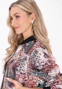 Bunte Bomberjacke mit Tiermotiven und Blumenmustern. Schwarzer Rippkragen. Große, runde, mehrfarbige Creolen.