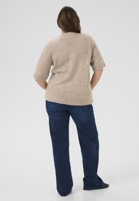 Pull court beige à manches courtes avec une finition texturée, ourlet côtelé, associé à un jean en denim bleu foncé. La tenue présente une coupe décontractée.