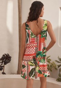 Klänning med blommönster och låg V-ringning bak, med livfulla färger som rött, grönt och orange i ett texturerat tyg och lös passform.