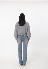 Grauer gestrickter, verkürzter Pullover mit strukturierten Ärmeln, kombiniert mit hochtaillierten, hellblauen Jeans. Sichtbare Gesäßtaschen und weit geschnittenes Design.