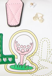 Patch en cuir rose, petite épingle dorée de chariot de golf, fleur blanche avec centre doré et illustration colorée de balle de golf sur fond blanc.