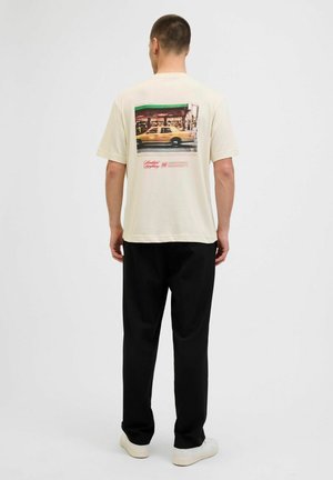 Cream cotton t-shirt featuring a colorful graphic print of a taxi on the back, paired with black trousers and white sneakers.