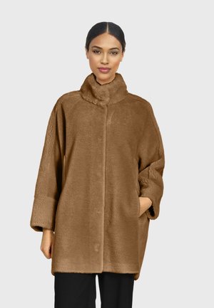 Manteau en fourrure brune avec un col haut, coupe décontractée et poches latérales. Il présente une texture douce et une fermeture frontale sans couture.