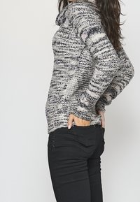Pull tricoté gris et noir avec un col bénitier, manches longues et motif texturé ; associé à un jean noir slim.