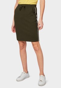 Zelená pletená sukně olivové barvy s páskem na stažení a bočními detaily v kontrastních barvách. Kombinováno s bílými teniskami a žlutým pruhovaným topem.