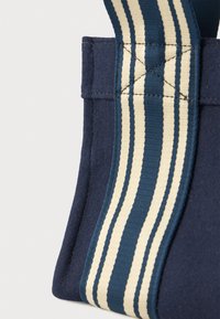 Κοντινό πλάνο της γωνίας μιας ναυτίλιας μπλε τσάντας με φαρδιά λευκή και μπλε ριγέ λουρί ραμμένο σε σχήμα Χ.