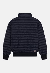 Veste matelassée bleu marine avec coutures horizontales, poignets et ourlet côtelés, col montant et petit logo circulaire en bas à droite dans le dos.