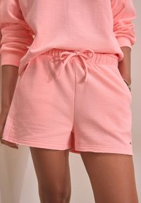 Shorts roses texturés avec une taille élastique et un cordon de serrage, dotés de poches latérales, conçus pour le confort et le port décontracté.
