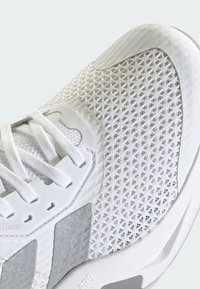 Hvid sportssko med et mesh-øvre lag, teksturerede detaljer og snørelukning. Bemærkelsesværdige reflekterende elementer og en formet gummisål.