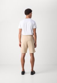 Beiga shorts i mjukt tyg med en avslappnad passform och en bakficka, ihop med en enkel vit t-shirt. Svarta skor fulländar outfiten.