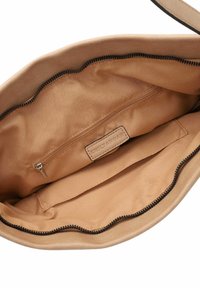 Interno di una borsa a tracolla in pelle beige, con una morbida foderatura in tessuto, dotato di una tasca con zip e un'etichetta del marchio impressa. Bordo della zip testurizzato.