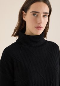 Pull à col roulé noir avec un motif texturé, doté d'un col haut et d'une coupe décontractée, fabriqué à partir d'un matériau doux et chaud.
