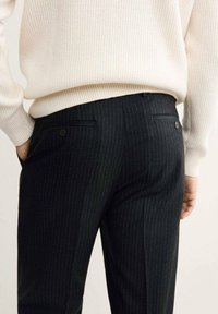 Pantaloni neri a righe verticali con una vestibilità su misura, dotati di due tasche posteriori e una texture liscia, abbinati a un maglione leggermente a costine.
