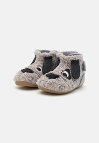 Pantofole in pile grigio con design di un cane, che presentano accenti neri su orecchie e naso, texture morbida e suola in gomma per una migliore aderenza.
