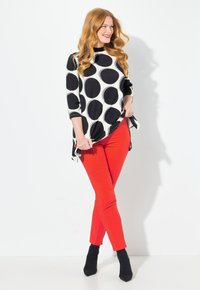 Černobílé tričko s puntíky a třičtvrtinovými rukávy v kombinaci s uplými červenými kalhotami a černými kotníkovými botami. Hladká, elastická látka.