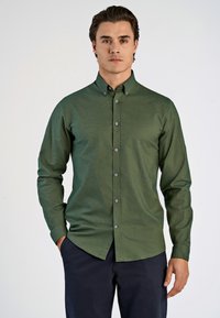 Camisa verde de algodón con textura, con cuello, mangas largas y botones grises en la parte delantera.
