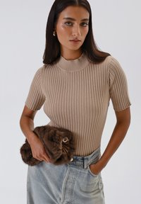 Top corto a maniche corte beige a coste con collo alto, abbinato a una pochette di pelliccia marrone in morbido peluche con dettagli in oro.