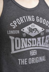 Sivi majica bez rukava izrađena od pamuka, s velikim bijelim grafičkim uzorkom koji sadrži tekst "Sporting Goods" i logotip lava. Jednostavan okrugli izrez.