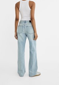 Světlomodré široké džíny s vysokým pasem, které mají dvě zadní kapsy a jemné omakání, kombinované s bílým těsným topem.
