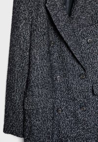 Cappotto doppiopetto in un motivo a spina di pesce bianco e nero, tessuto in lana texturizzata, con grandi bottoni e un ampio colletto.