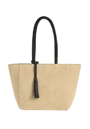 Sac cabas en daim beige avec poignées tressées noires et détail pompon noir suspendu à une poignée.