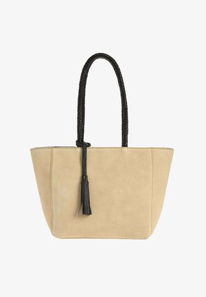 Sac cabas en daim beige avec poignées tressées noires et détail pompon noir suspendu à une poignée.