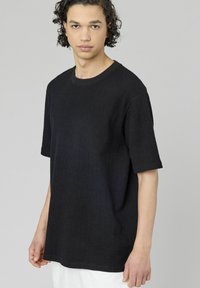T-shirt noir à manches courtes et col rond, avec une coupe légèrement ample et un tissu texturé. Ourlet propre et détails minimalistes.