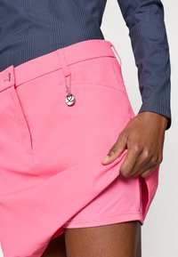 Rózsaszín sportnadrág sima textúrával, elülső zsebbel, övvel ellátott derékkal és fém kedvességgel.