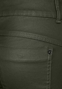 Olivgrön denimbyxor med tajt passform, stora fickor och mörka sömmar. Inkluderar en liten logo nära fickan. Slät textur.