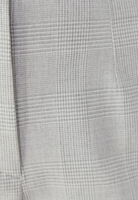 Zbliżenie szarej i białej tkaniny w kratkę z subtelnym wzorem houndstooth i widocznymi szwami.