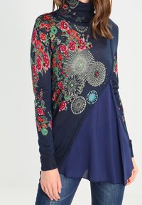 Marineblauer Rollkragenpullover mit floraler Stickerei in Rot, Grün und Aqua. Verfügt über ein geschichtetes Design mit einem blauen Chiffon-Unterteil.