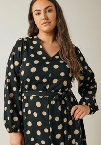 Schwarzes Kleid mit goldenen Punkten, V-Ausschnitt, lange Ärmel, Knöpfe entlang der Vorderseite, tailliert mit passendem Bindegürtel, strukturierter Stoff.