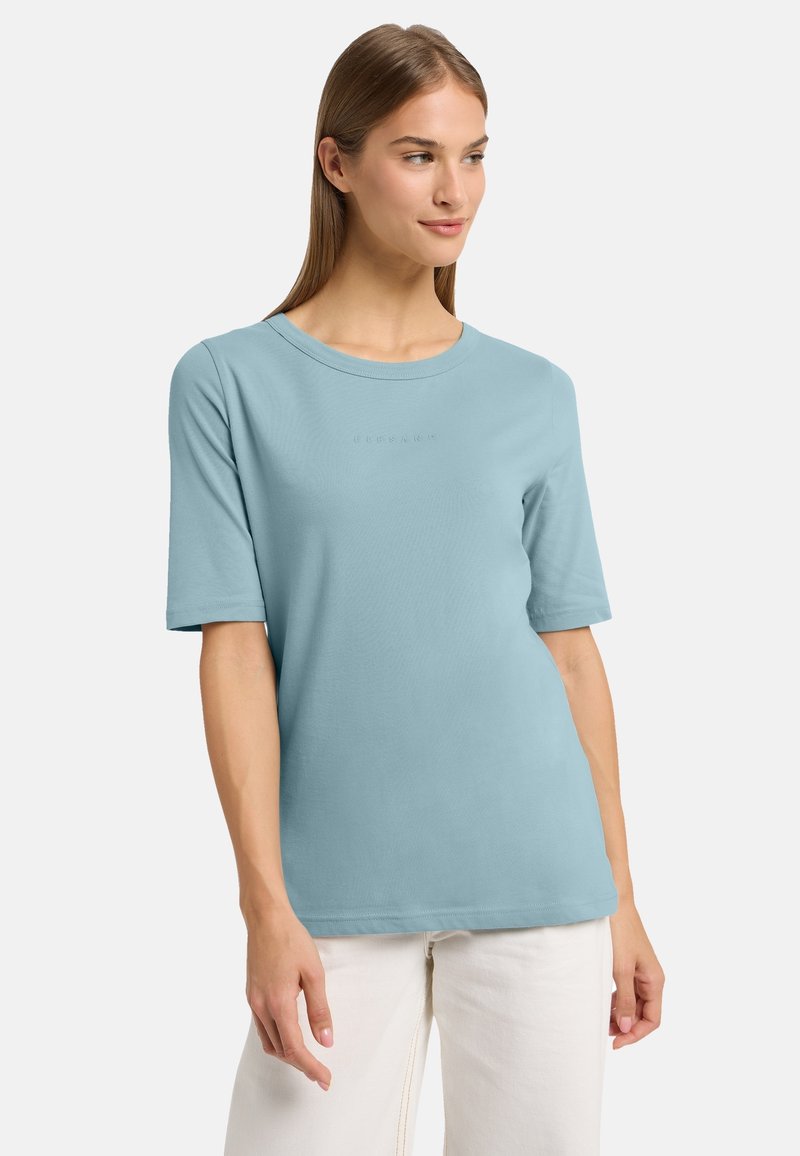 Tricou scurt cu mâneci, de culoare albastru deschis, realizat dintr-un material moale, cu decolteu rotund și un detaliu subtil cu logo embosat pe față.