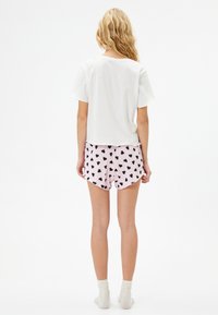Valkoinen lyhythihainen crop-top, joka on yhdistetty vaaleanpunaisiin shortseihin, joissa on mustia sydäntulosteita. Sukat ovat ivory-väriset ja nypyröidyt.