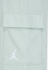 Mintgrøn cargobukse-stof med en stor klaplomme, med hvid syning og et hvidt Jumpman-logo syet nær lommen.